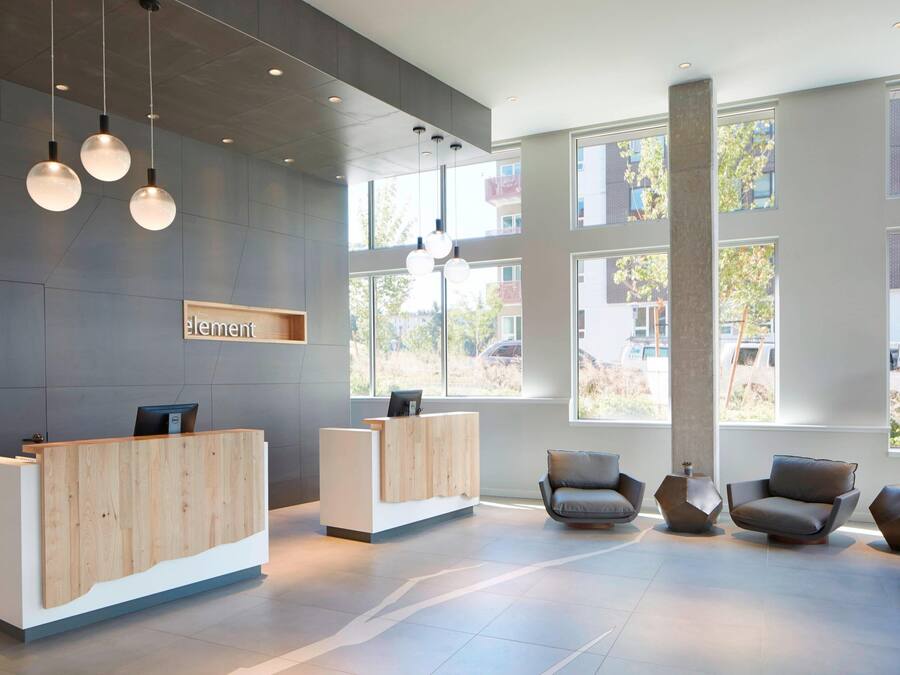 A modern reception area with a wooden reception desk, two seating areas with contemporary chairs, and large windows allowing natural light.