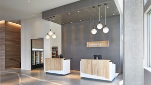 A modern reception area with two wooden reception desks, a wall-mounted display, and hanging pendant lights. - Element by Marriott Seattle Redmond (Redmond)