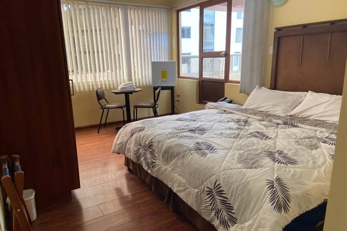 Una habitación de hotel con una cama grande, un escritorio con una silla y una ventana con persianas.