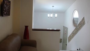 Una sala de estar moderna con suelo de mármol, un sofá marrón, un jarrón rojo y una escalera con un espejo redondo.
