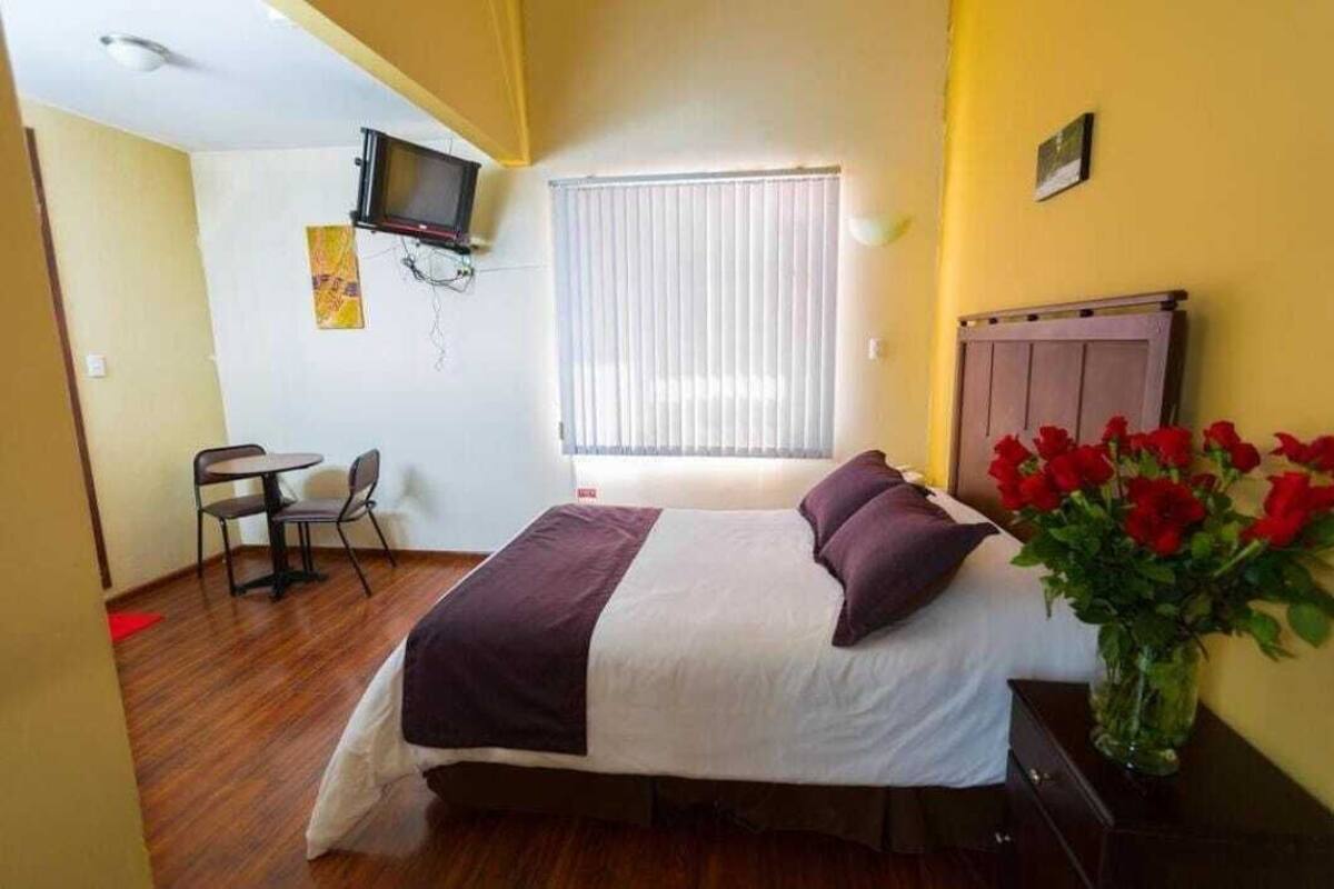Un dormitorio con cama, escritorio, silla, televisor y ventana con persianas.