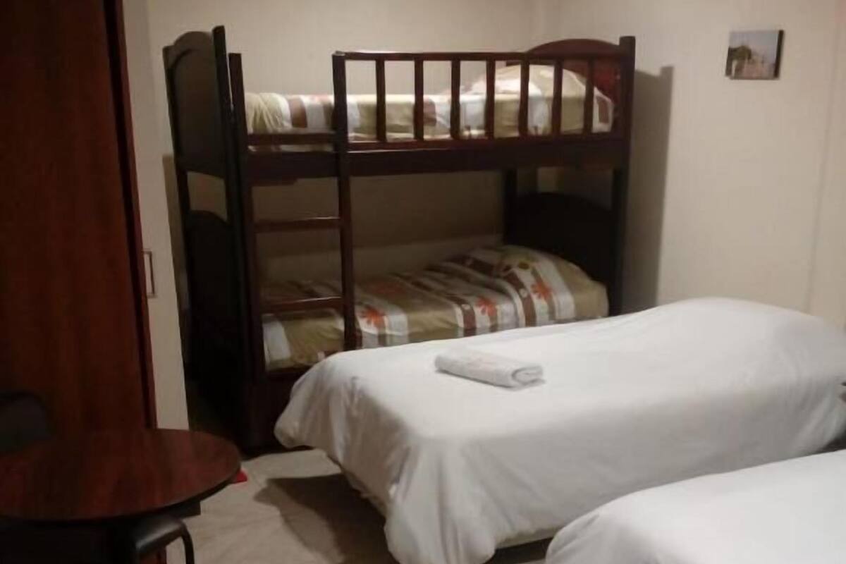 Una habitación con dos camas individuales, una litera de madera, un escritorio con silla y suelo de baldosas.