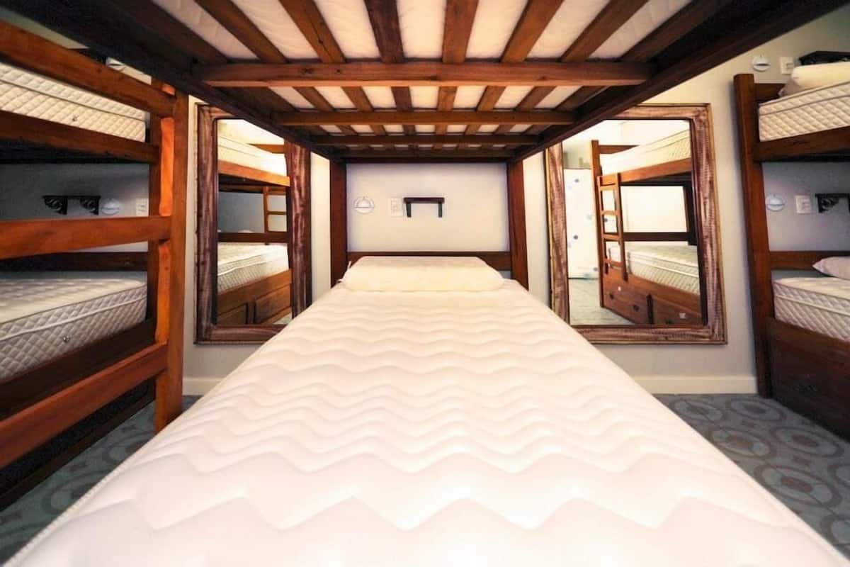 A bunk bed room with a central bed, wooden beams, and a small window.
