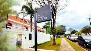 Un hostal llamado 'Hostel Poesia' con un letrero, un camino pavimentado, coches estacionados y un edificio blanco con techo rojo.