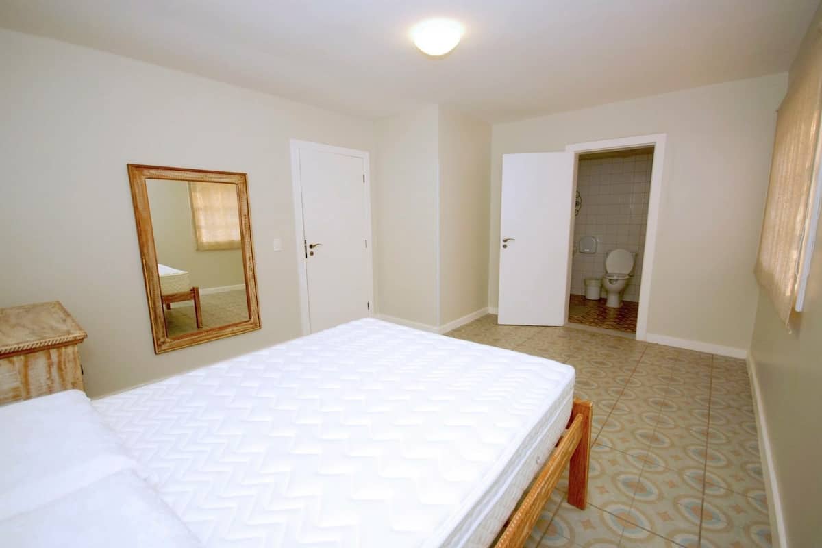 A bedroom with a bed, a mirror, and a door leading to a bathroom.