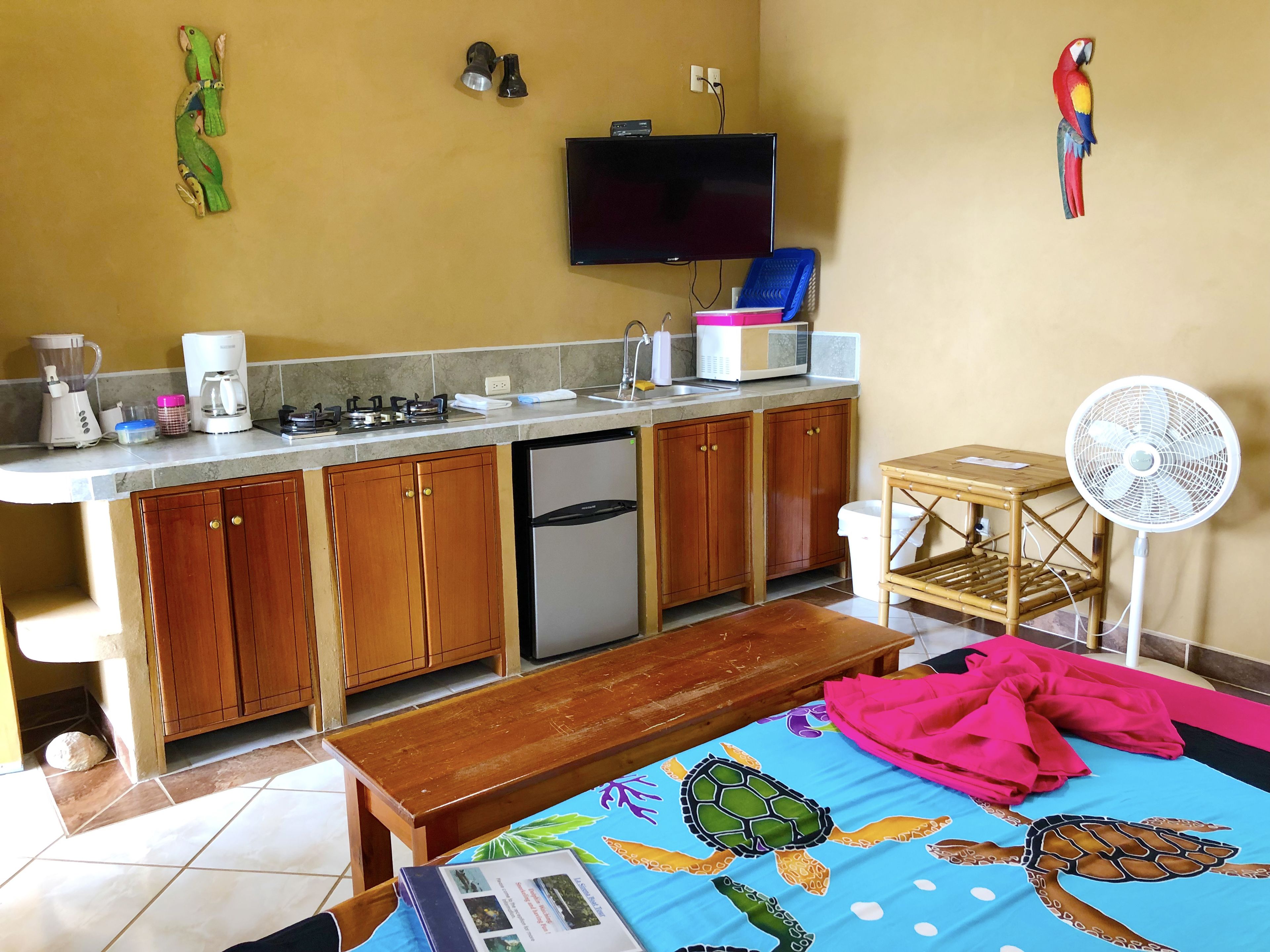 A compact kitchen with wooden cabinets, a built-in microwave, and a sink. There's a bench and a table with a turtle-themed tablecloth.