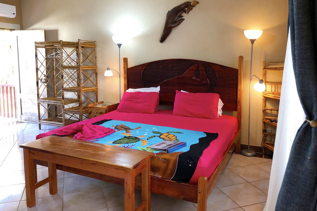 A room with a wooden bed, a bedside table, a wall-mounted shelf, and two bedside lamps.