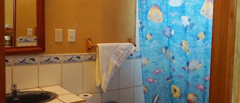 Een badkamer met een wastafel, toilet en douchegordijn met een visdessin.
