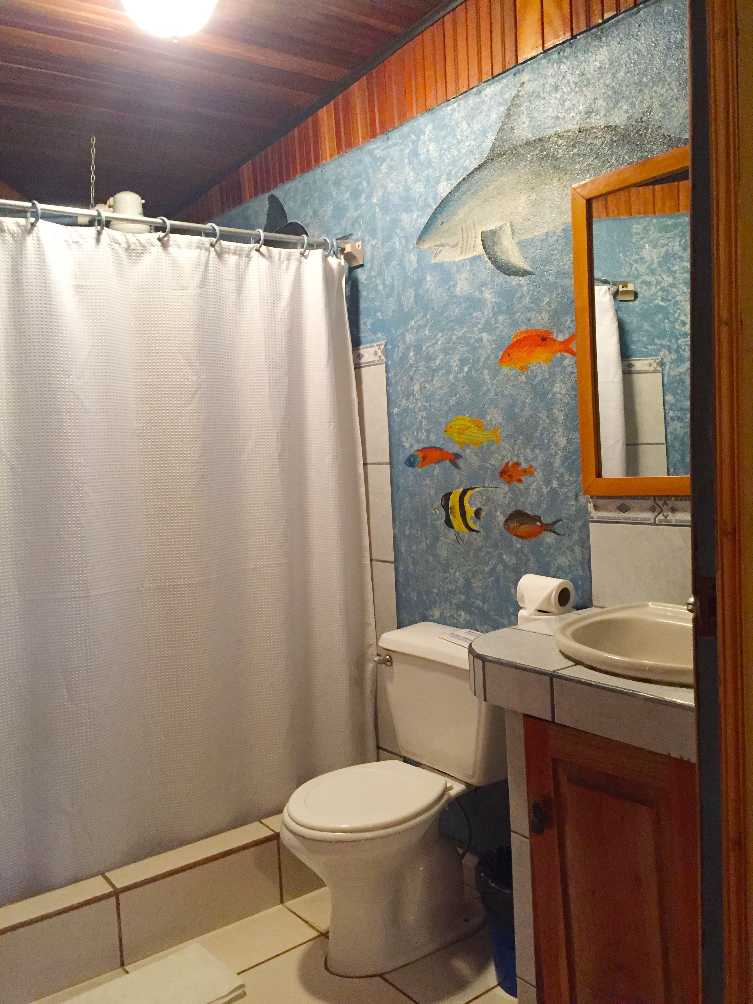Un baño con cortina de ducha, inodoro, lavabo y un mural de peces en la pared.