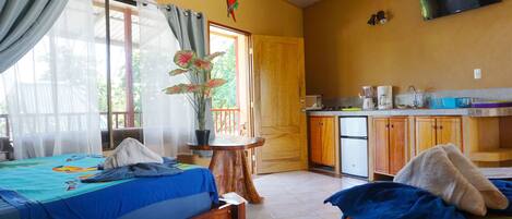 Una habitación con dos camas, una pequeña cocina y una ventana con cortinas.