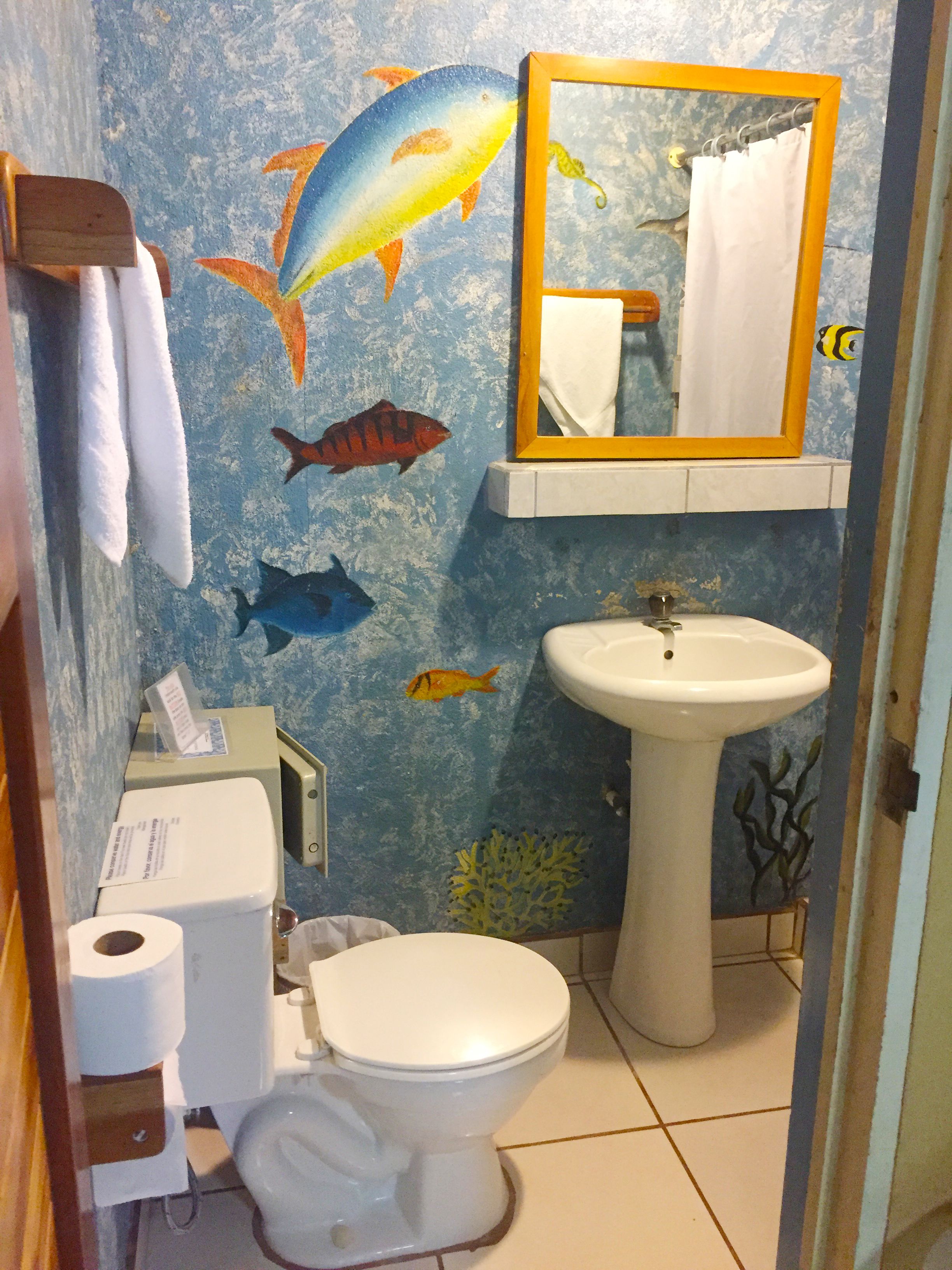 A bathroom with a toilet, sink, and a wall mural of fish.