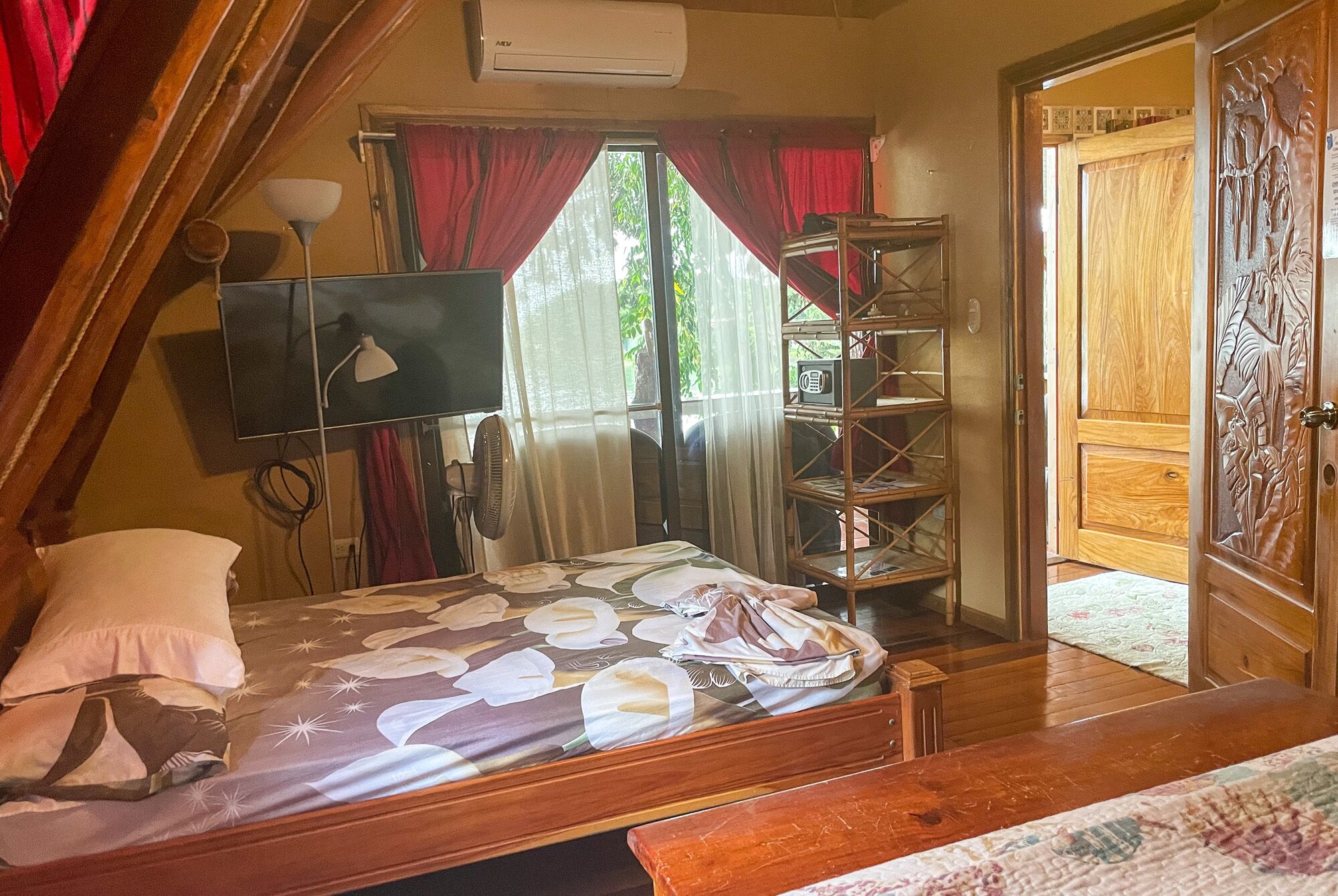 Un dormitorio con una cama, televisión, ventilador y una puerta de madera con diseño tallado.