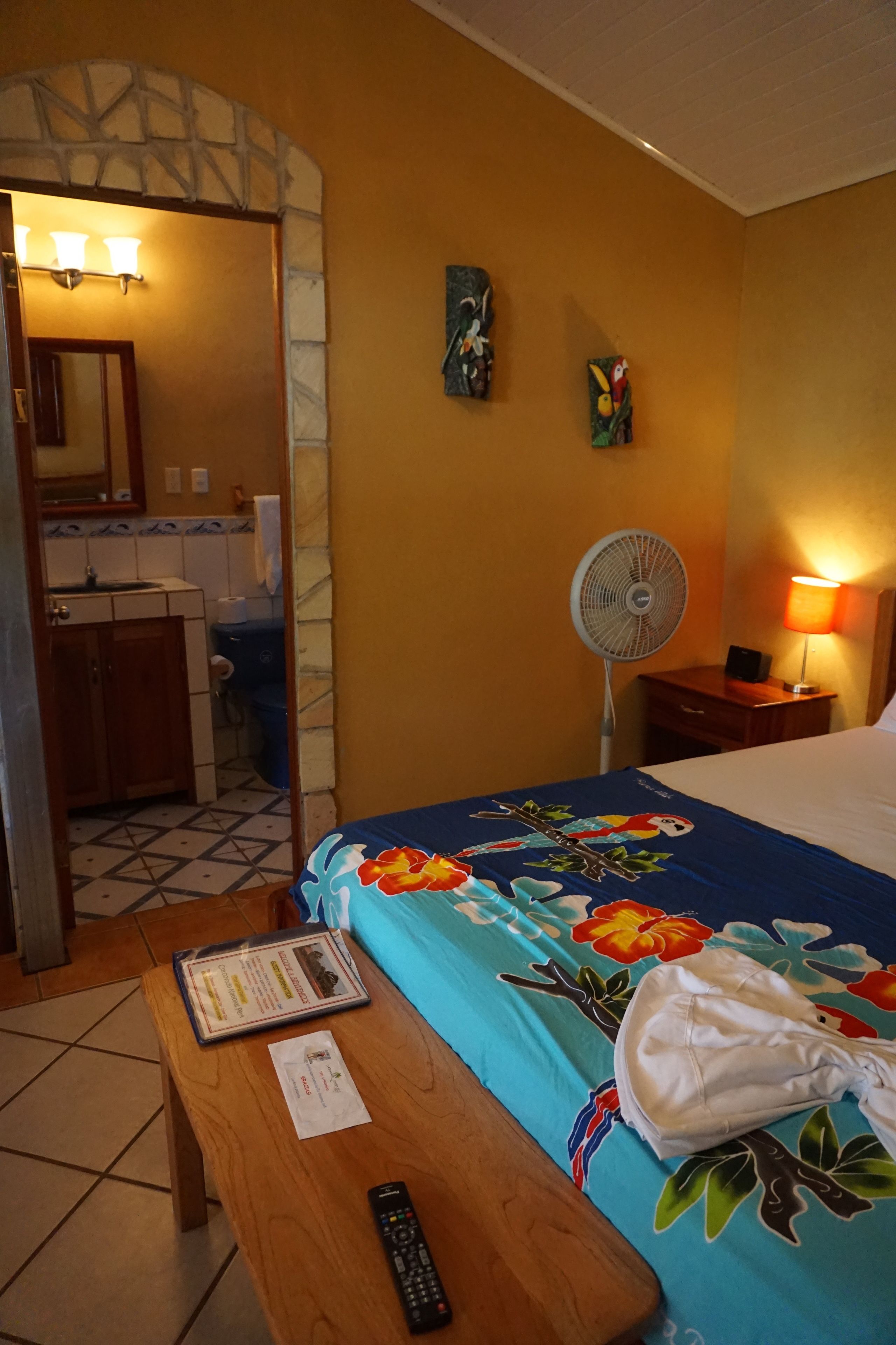 Une chambre d’hôtel avec un lit, un bureau, un ventilateur et une salle de bain visible à travers une arche.