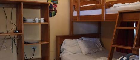 A bunk bed room with a TV, a fan, and a shelf unit.