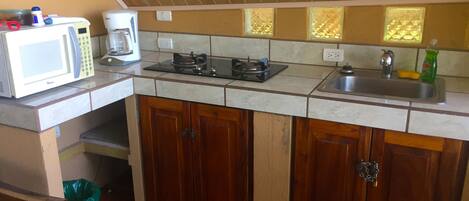 A compact kitchen with a microwave, stove, sink, and wooden cabinets.