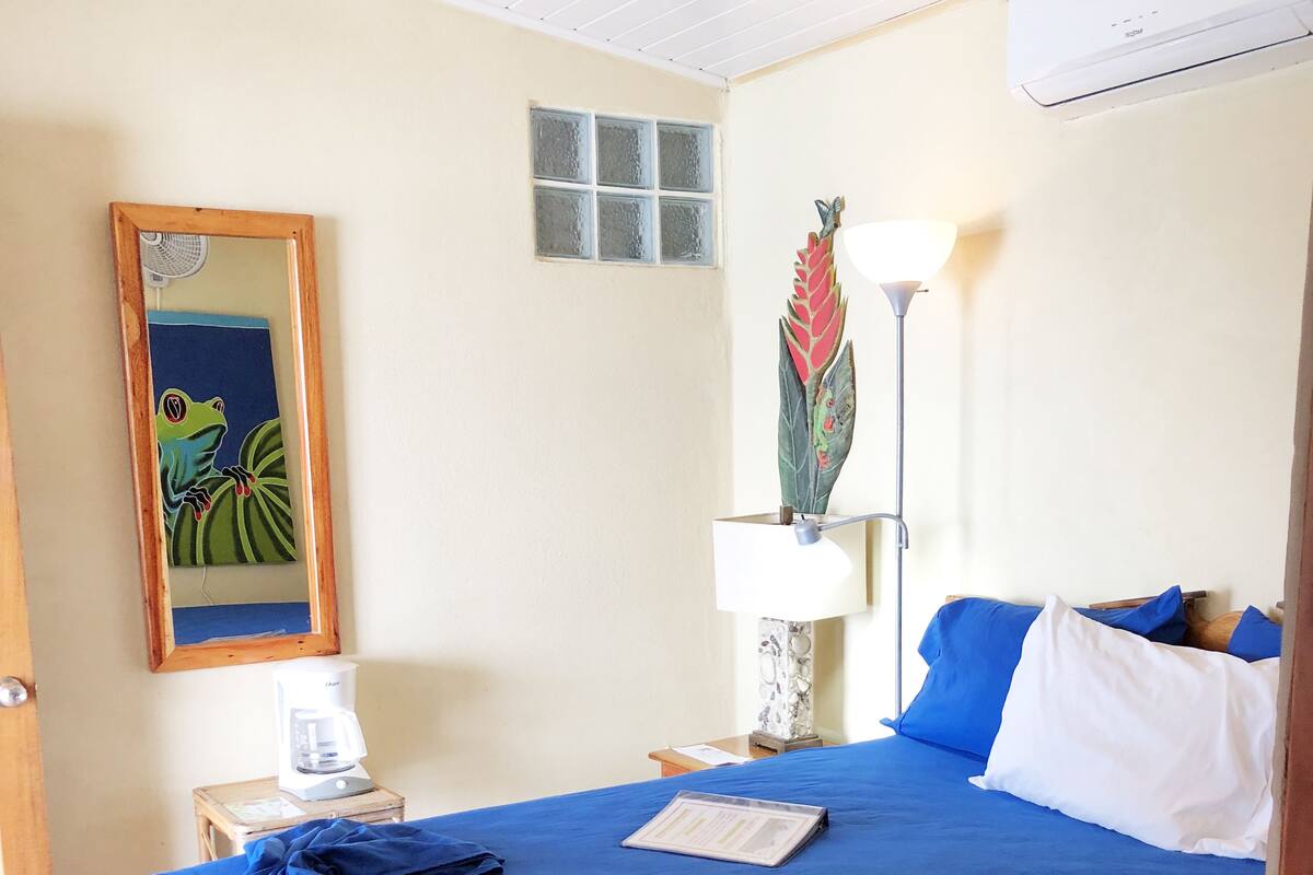 A neatly made bed with a blue bedspread, a lamp, and a framed picture on the wall.