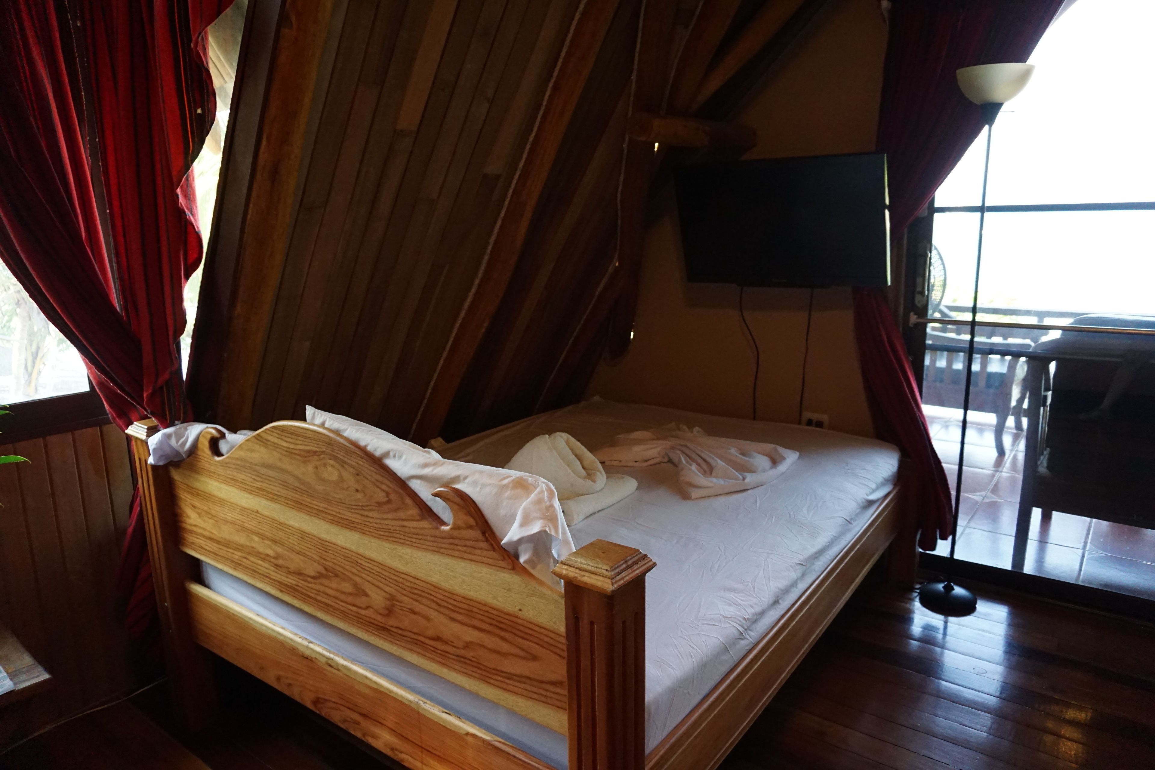 Ein hölzernes Bett in einem Raum mit schrägem Dach und einem an der Wand befestigten Fernseher.