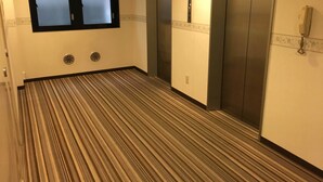A hotel corridor with a striped carpet, two elevators, and a phone on the wall. - Kashiwa Plaza Hotel (Kashiwa)
