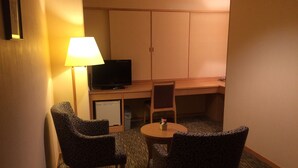 A hotel room with two patterned armchairs, a small round table, a television on a stand, and a desk with a chair. - Kashiwa Plaza Hotel Annex (Kashiwa)