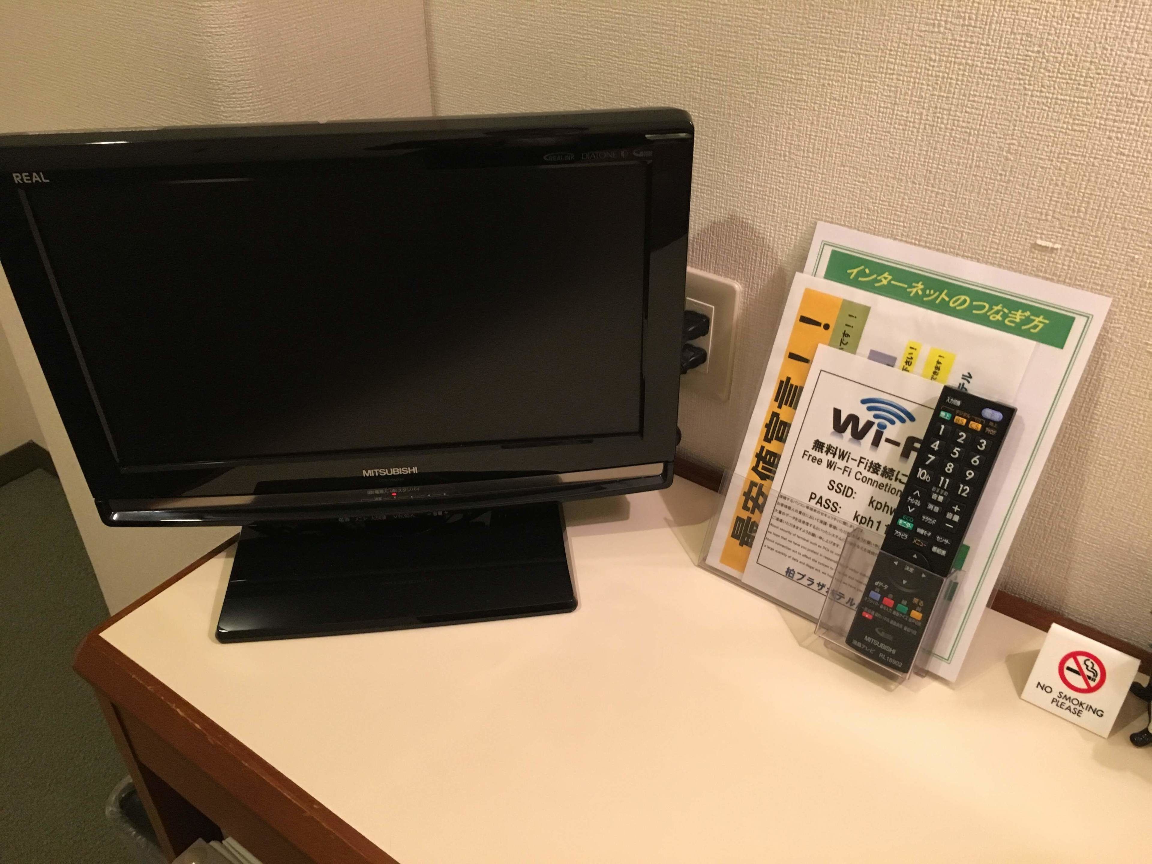 Uma TV Mitsubishi em um suporte, um código de acesso Wi-Fi e um aviso de proibido fumar.