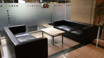 A modern lounge area with black leather sofas, a wooden coffee table, and a tiled floor.