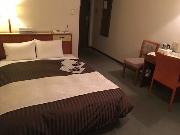Hotellihuone, jossa on suuri sänky, yöpöytä lampun kanssa, tuoli ja työpöytä tuolilla.