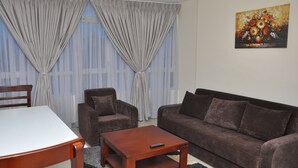 A living room with a brown sofa, two armchairs, a wooden coffee table, and a white table. - Afroaddis Hotel Apartment (Addis Ababa)