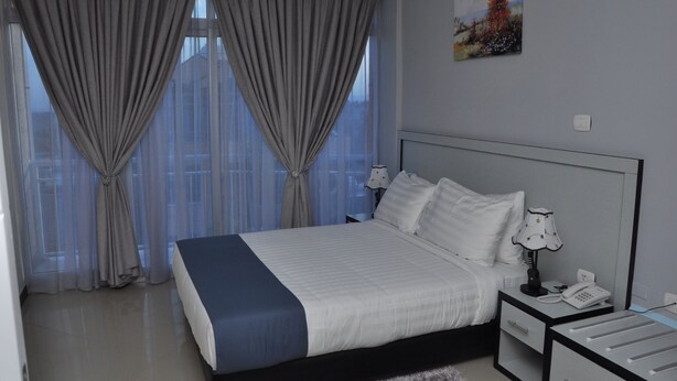 A hotel room with a large bed, a bedside table with a lamp, a phone, and a window with curtains. - Afroaddis Hotel Apartment (Addis Ababa)