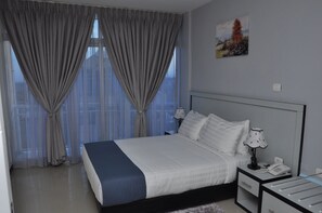 A hotel room with a large bed, a bedside table with a lamp, a phone, and a window with curtains.