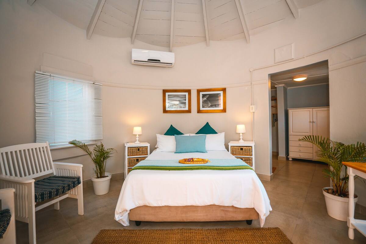 A bedroom with a bed, bedside tables, a chair, a potted plant, and a ceiling fan.