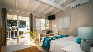 A bedroom with a bed, a desk, a chair, a TV, and a balcony with a potted plant. - Surf Motel (eMdloti)