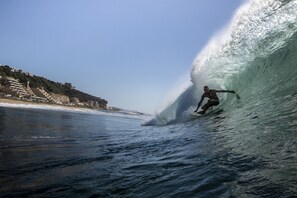 A surfer riding a large wave with buildings in the background. - Surf Motel (eMdloti)