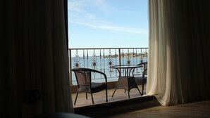Ein Balkon mit Tisch und Stühlen, der auf ein Gewässer und eine ferne Stadtansicht blickt.