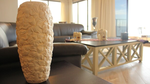 Ein Wohnzimmer mit einer großen, strukturierten Vase auf einem Tisch, einem Sofa und einem Couchtisch mit Kreuzgeflecht.