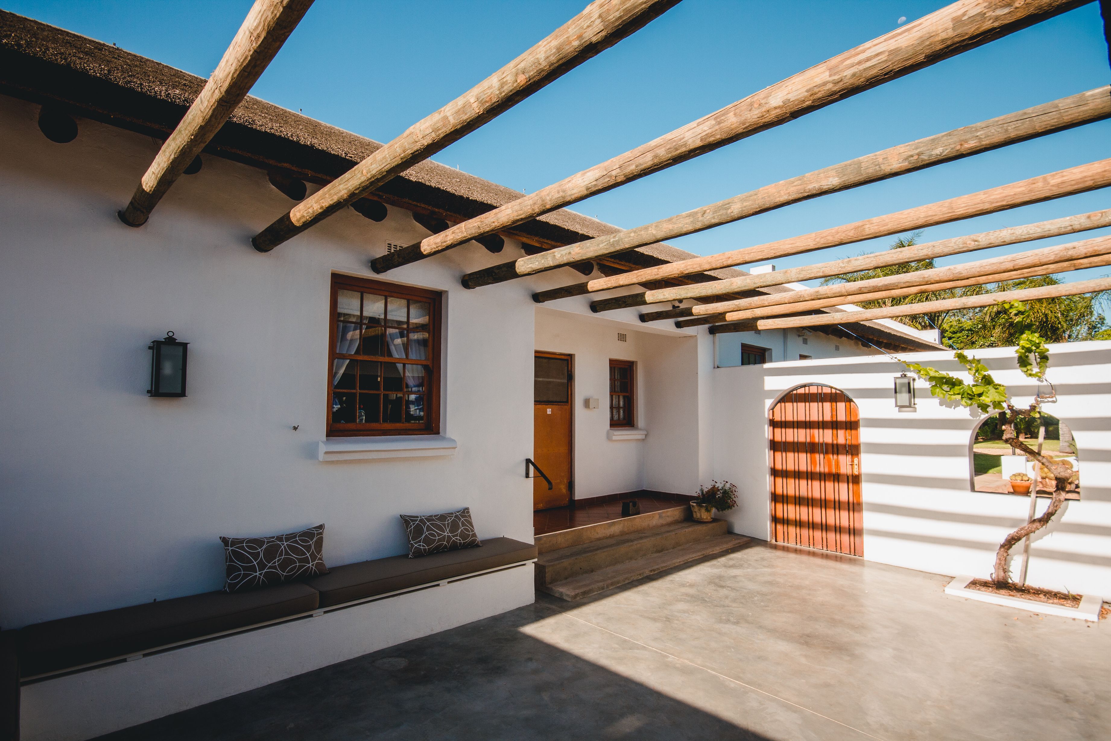 A white building with a wooden pergola, a bench, and a door.