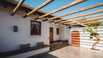 A white building with a wooden pergola, a bench, and a door.