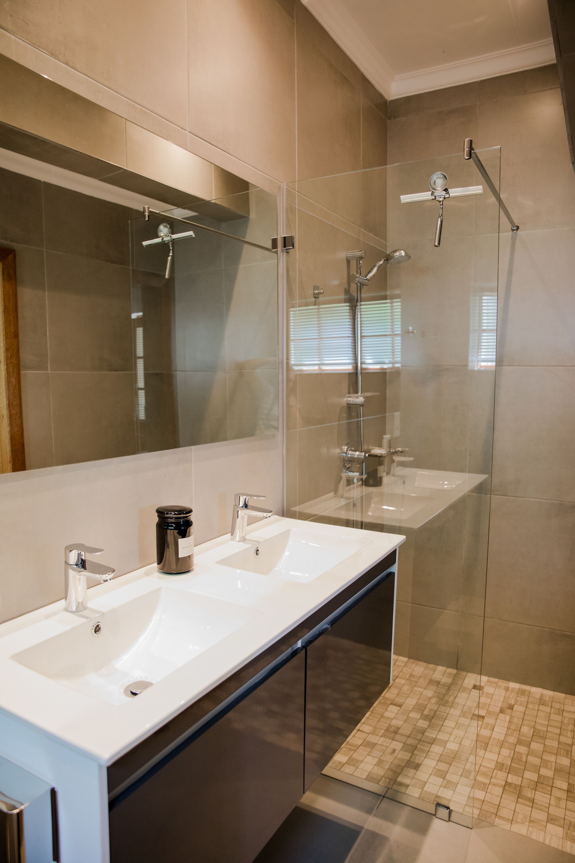 A modern bathroom with two sinks, a large mirror, and a glass-enclosed shower area.