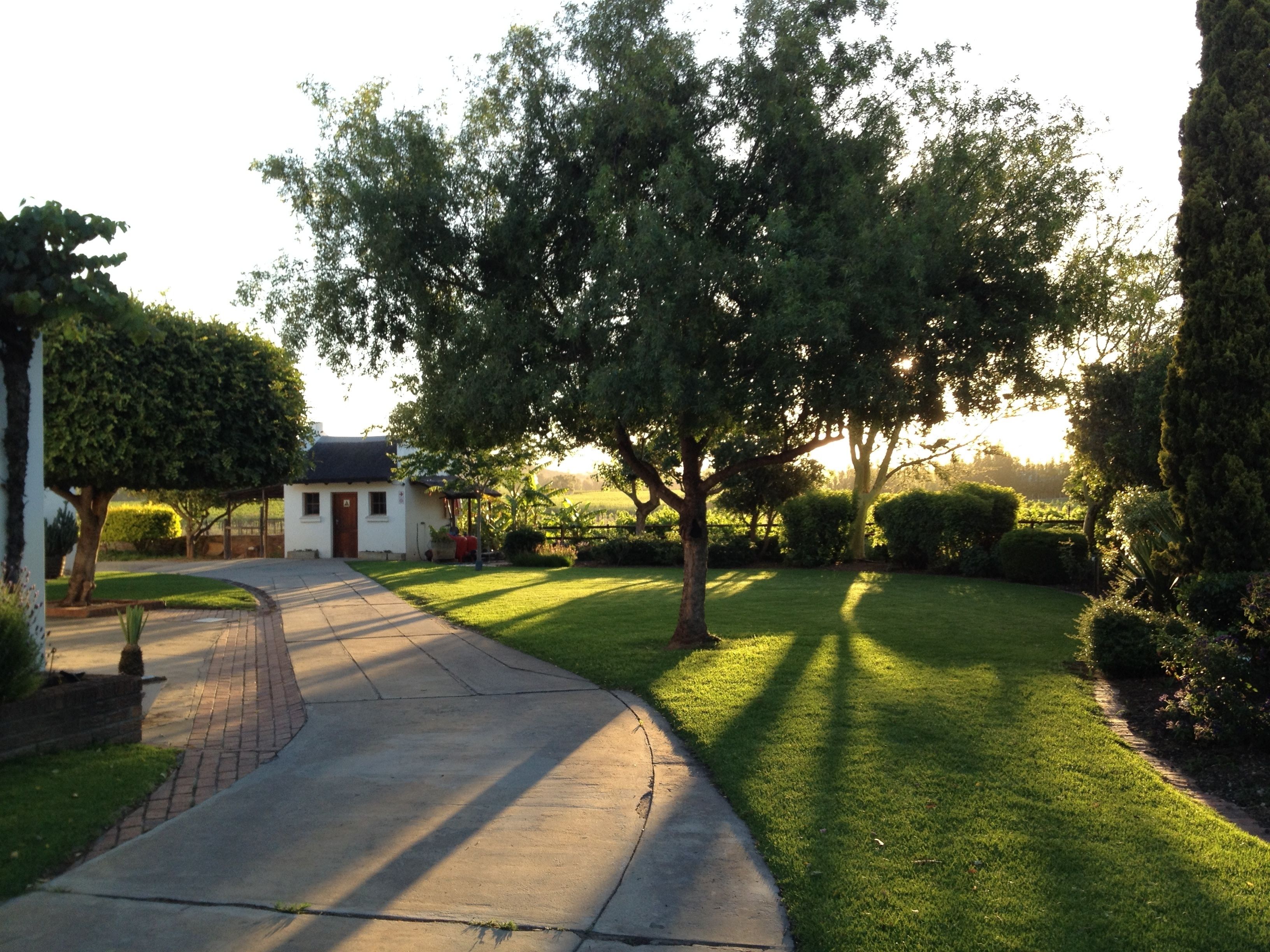 A residential property with a paved driveway leading to a white house, surrounded by well-maintained lawns and mature trees.