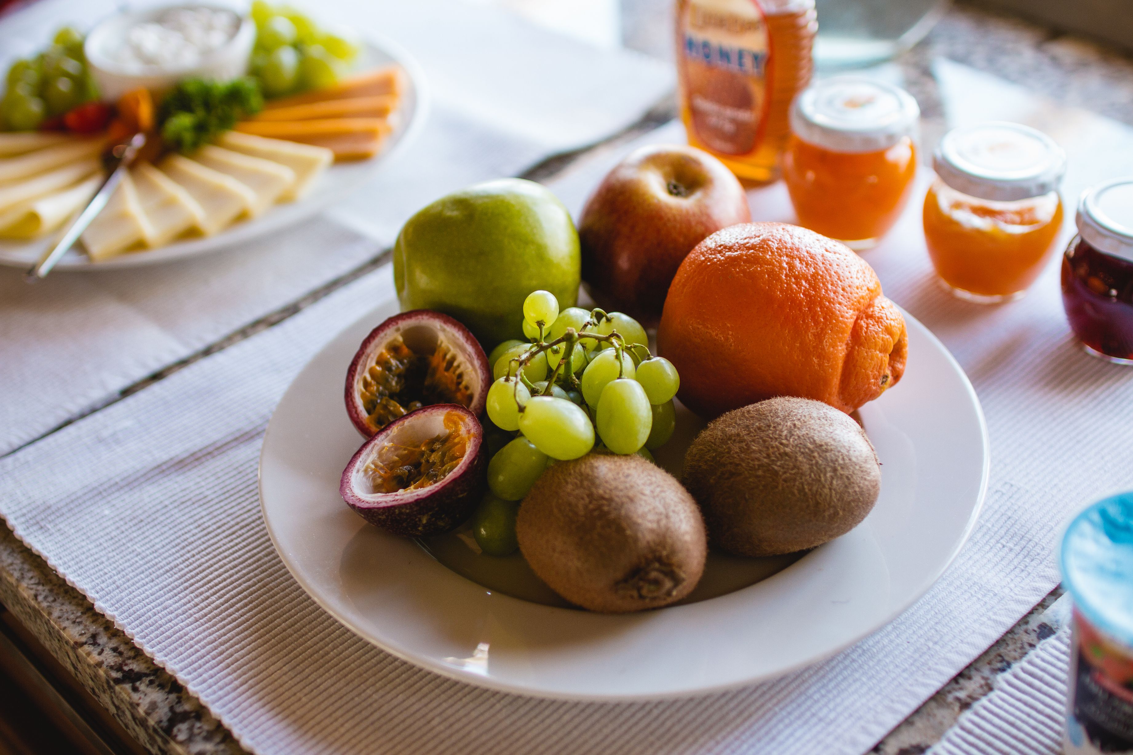 Un plato de frutas variadas y un tarro de miel sobre una mesa.