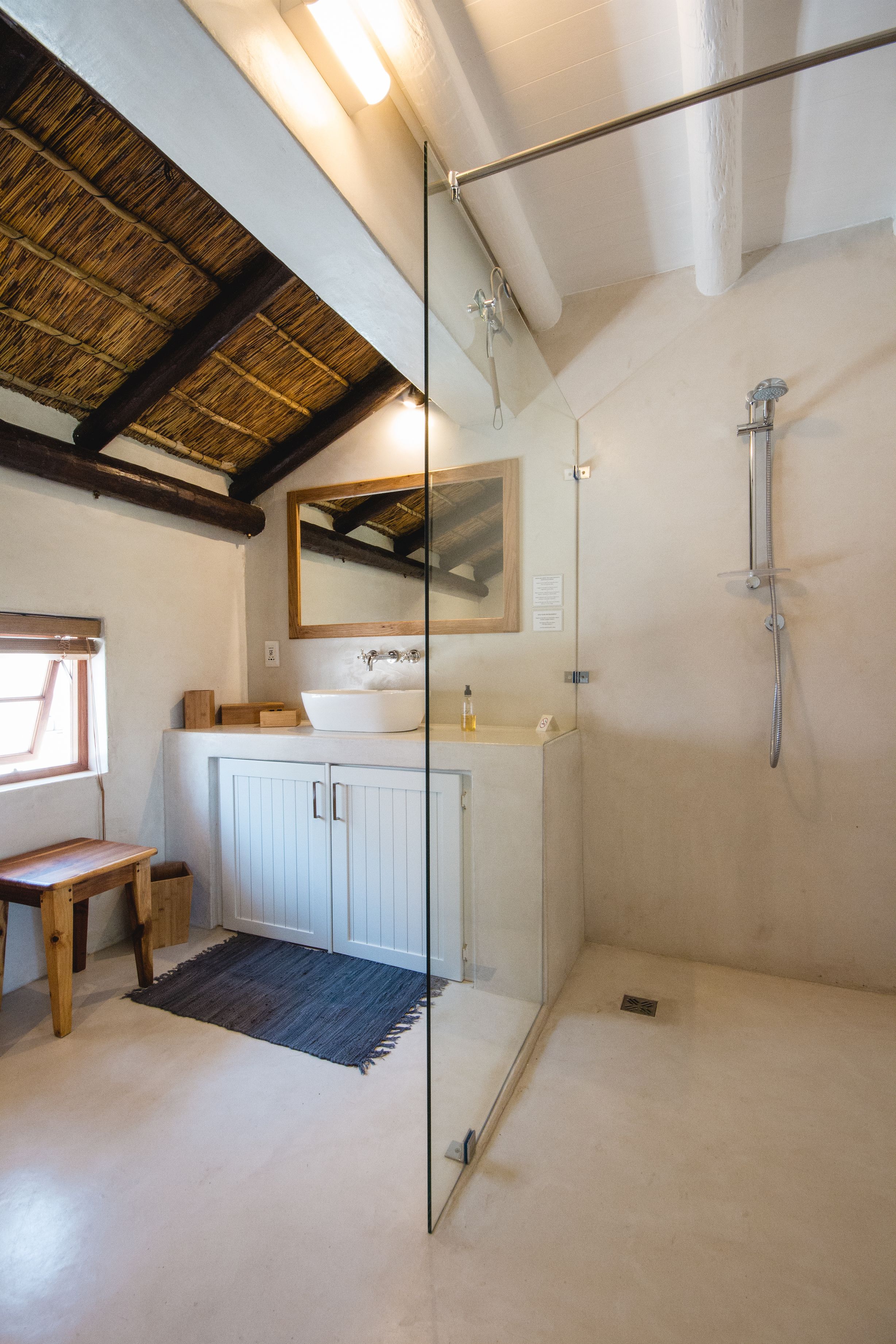 Une salle de bain avec une douche à parois de verre, un banc en bois, un lavabo blanc et un grand miroir.