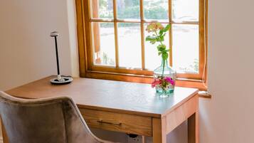 A wooden desk with a chair, a vase with flowers, and a lamp.