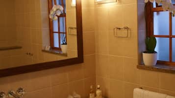 A bathroom with a large mirror, a sink, a window with a plant, and towels on the counter.