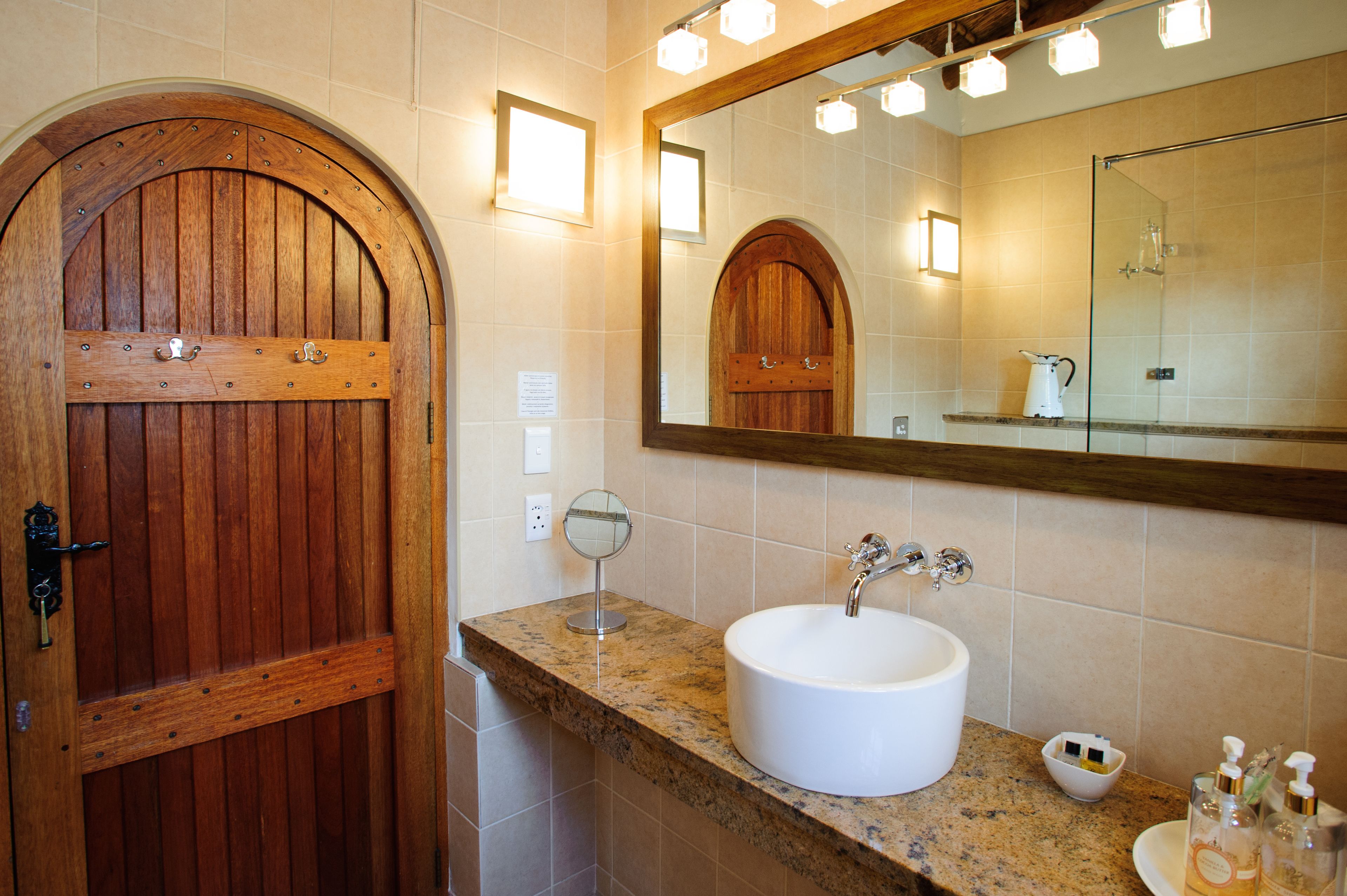 A bathroom with a wooden door, a sink with a mirror above it, and a shower area.
