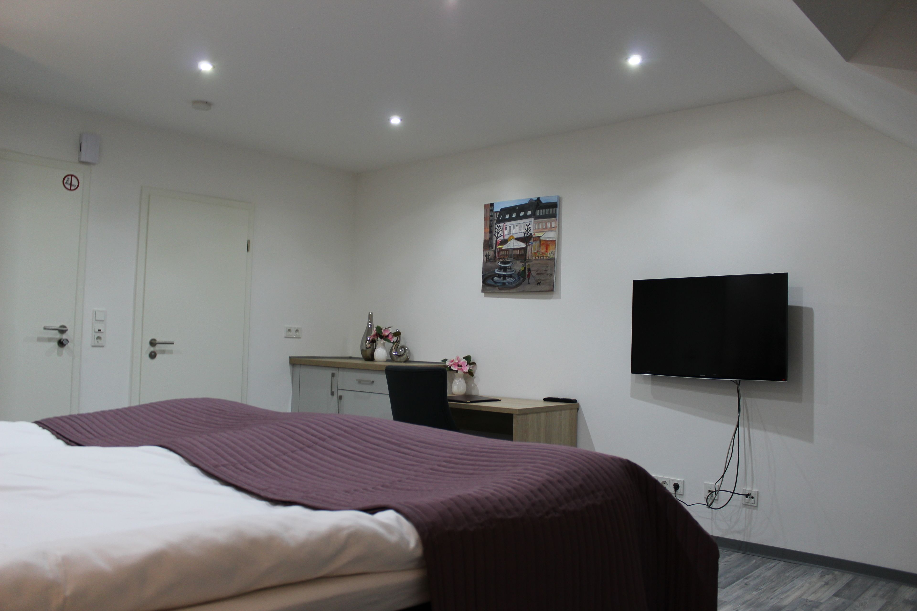 Una camera d'albergo con un letto, una scrivania, una sedia, una TV e un quadro appeso al muro.