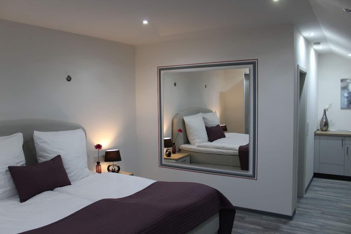 Una habitación de hotel moderna con una cama grande, una mesita de noche, un espejo y un pequeño escritorio con una lámpara.