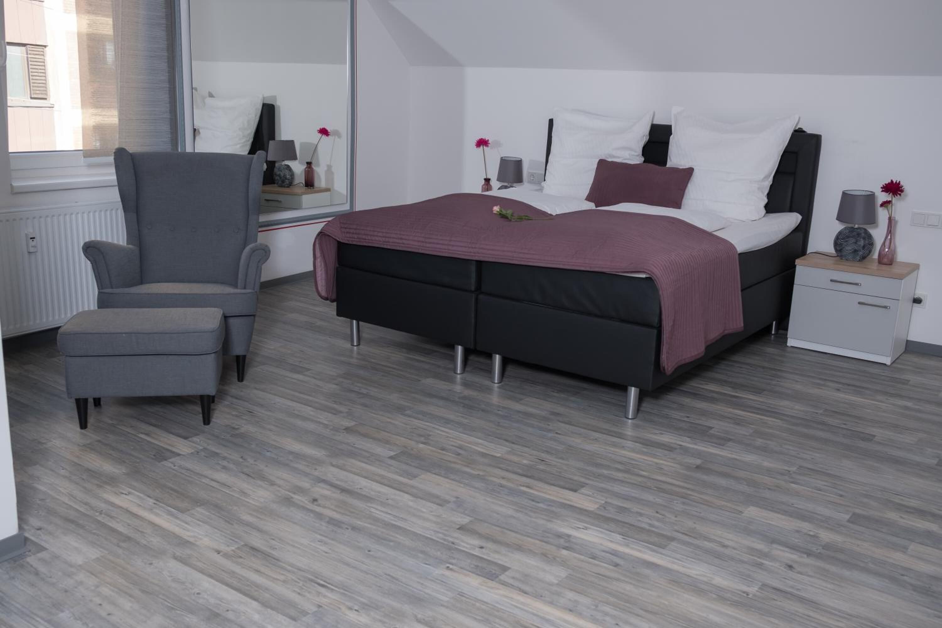 Un dormitorio moderno con cama, una silla, una mesita de noche y un espejo.