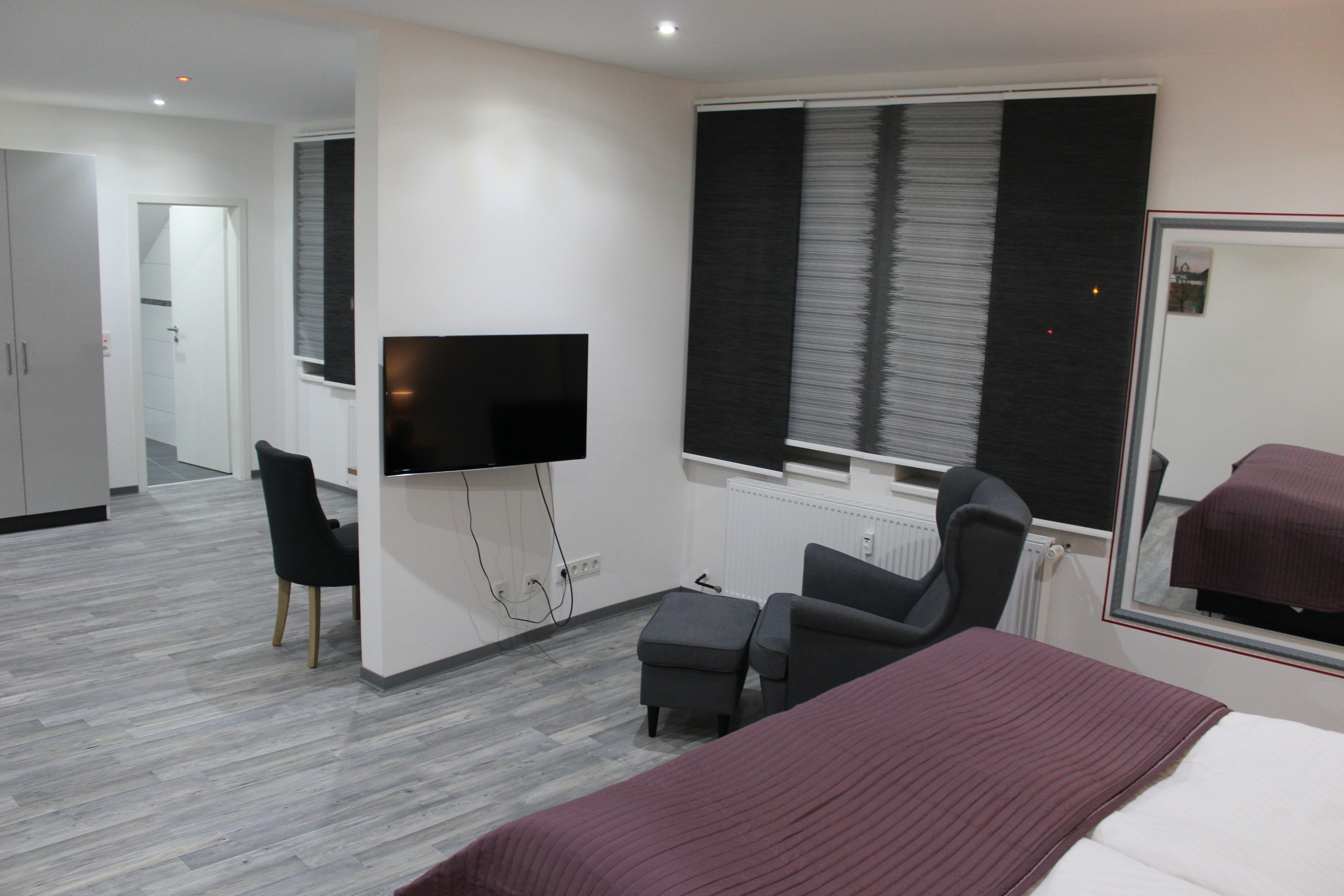 A modern hotel room with a bed, a TV, a desk, and a chair.