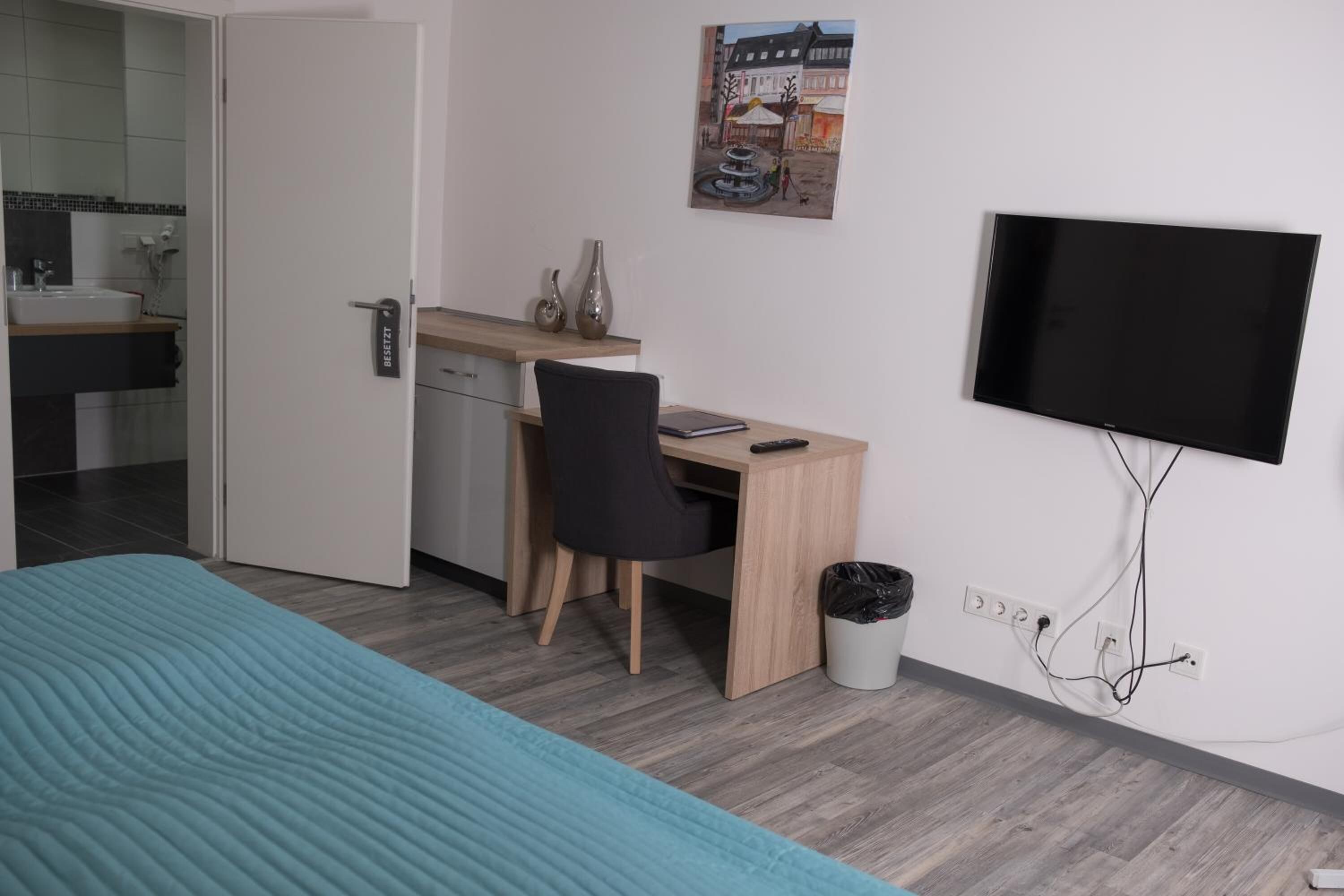 A hotel room with a bed, a desk, a chair, a TV, and a small trash bin.