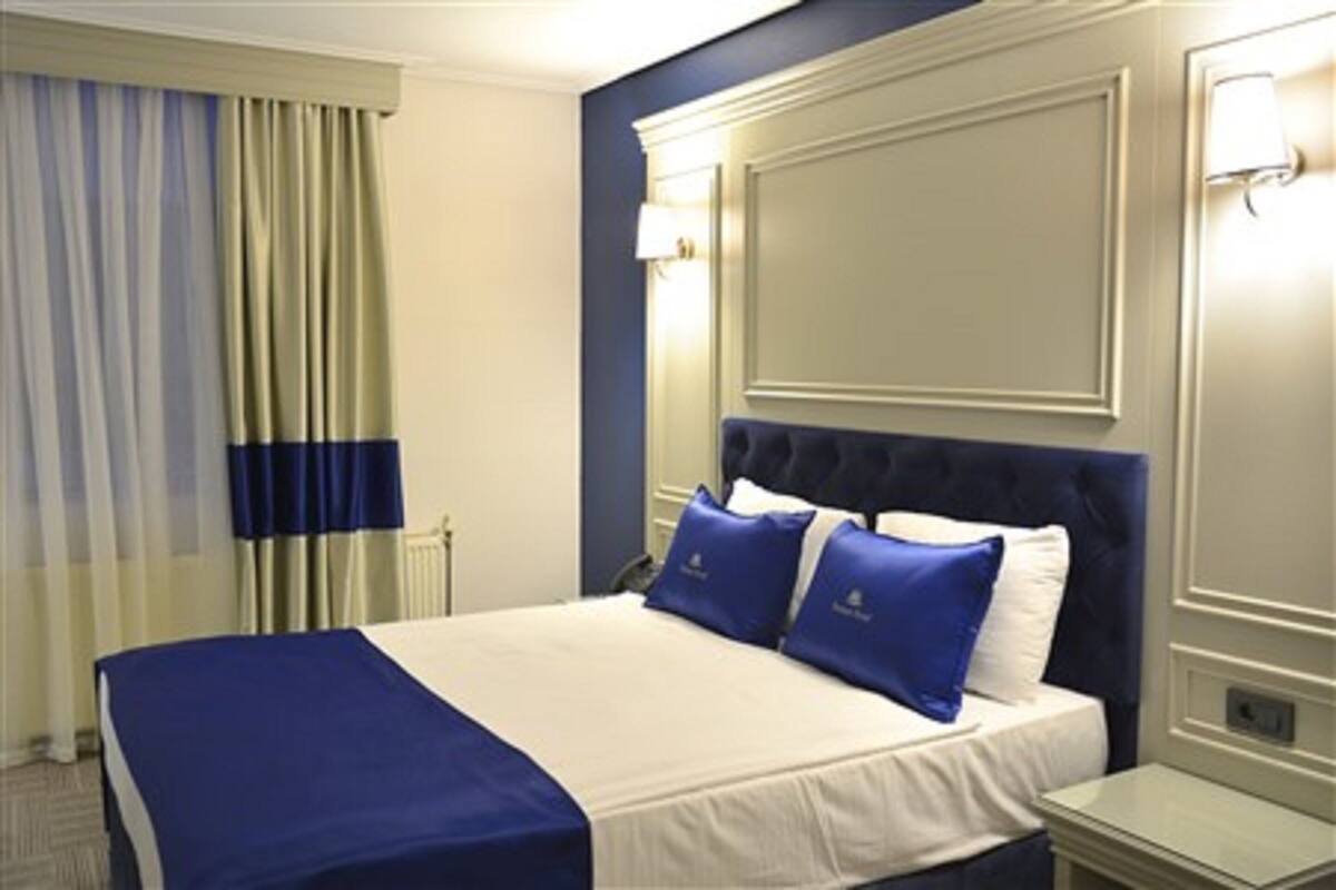 A hotel room with a large bed, a nightstand, a lamp, and a window with curtains.