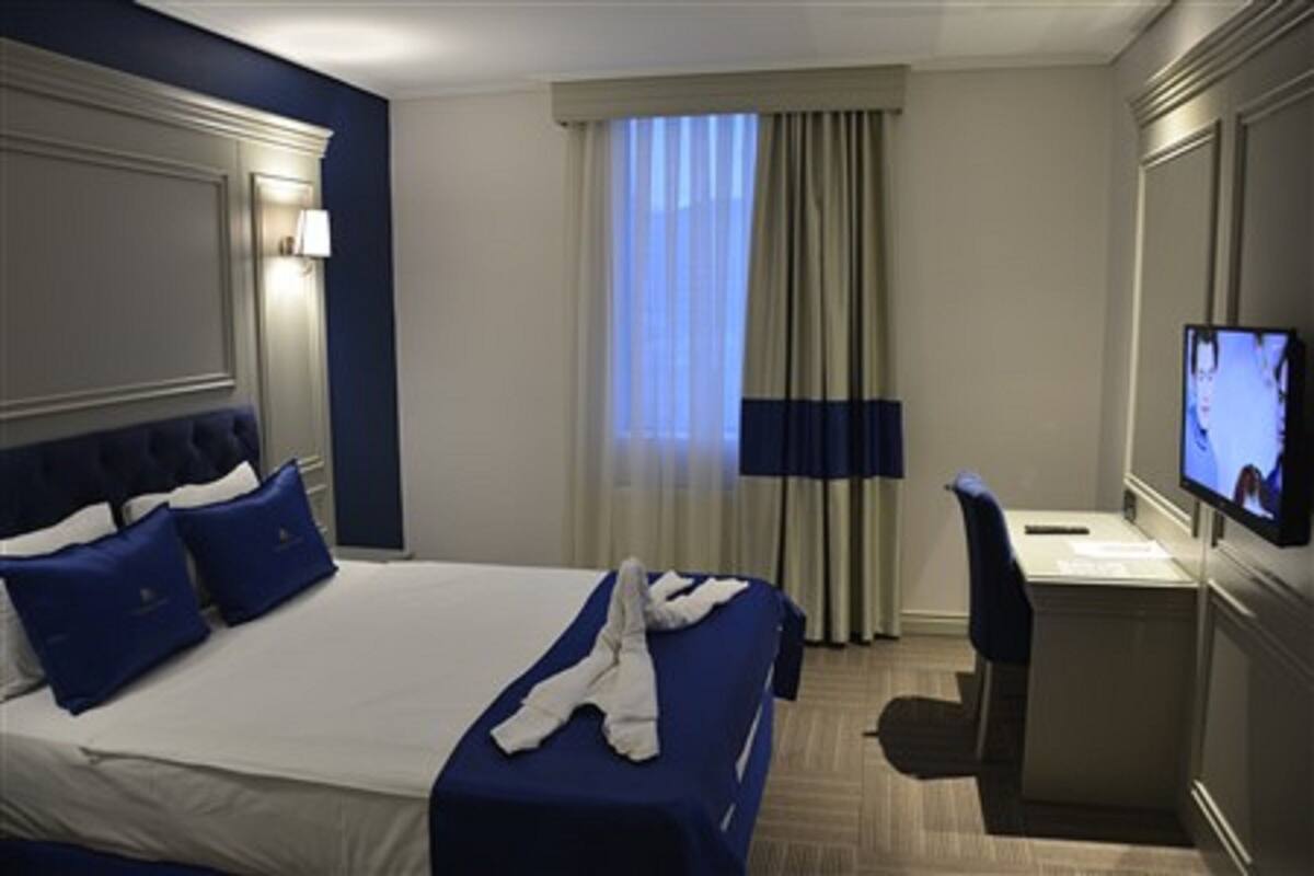 A hotel room with a large bed, a desk, a chair, and a TV on the wall.